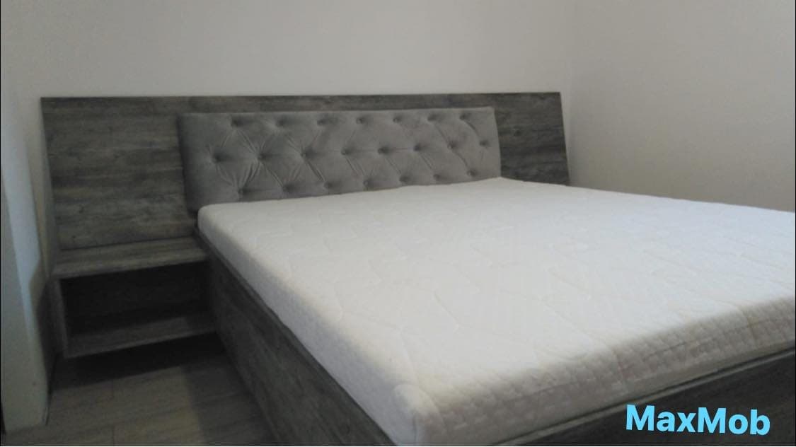 Pat cu tăblie gri capitonată încadrată de un panou în decor lemn
